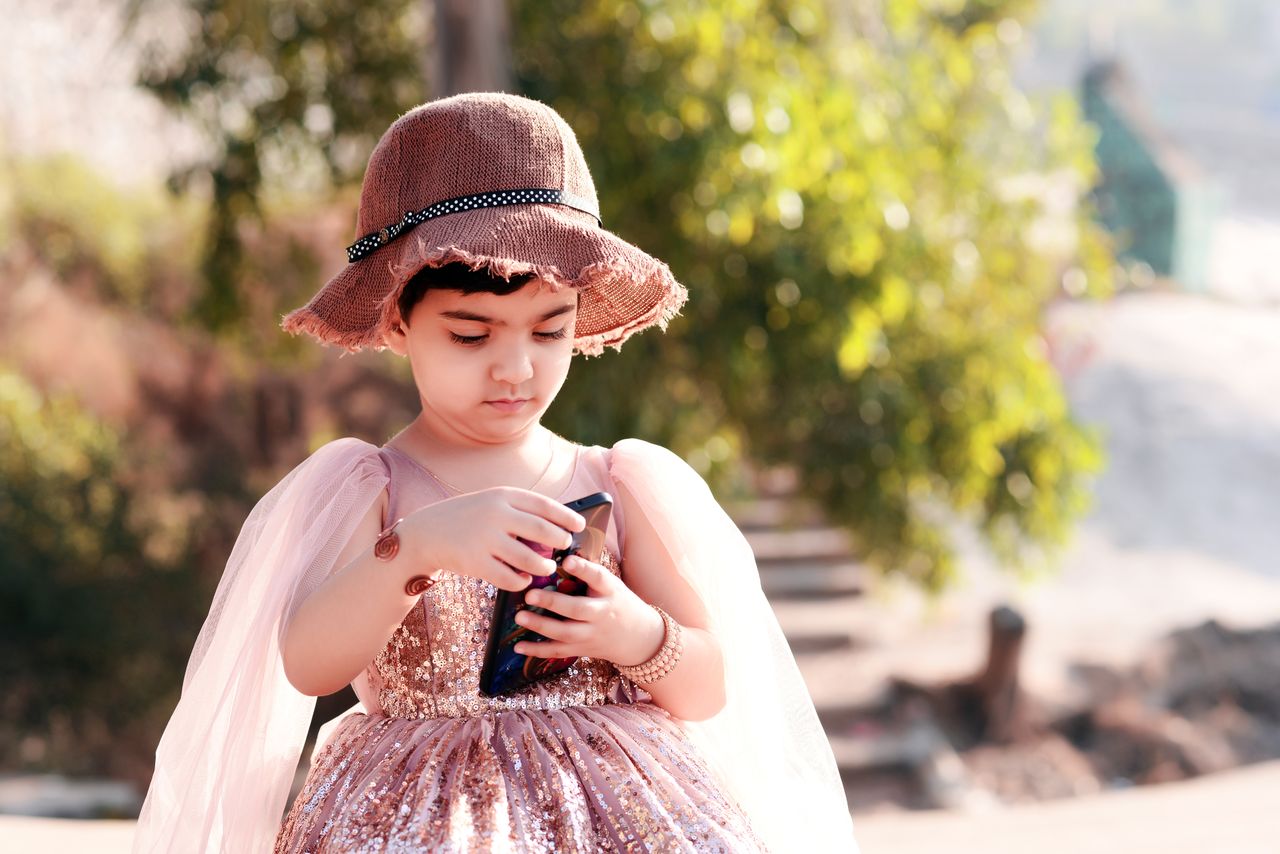 Mastering the First Impression: Your intriguing post title goes here A young girl wearing a brown hat and sequin dress uses a smartphone outdoors.